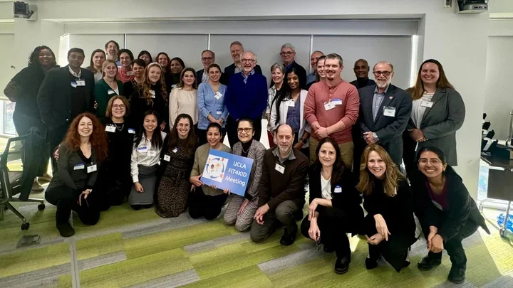 Large group photo of diverse professionals posing indoors, with one person holding a conference poster.