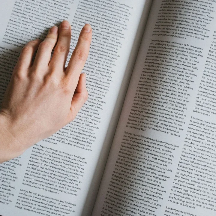 Hand resting on open book filled with dense text columns.