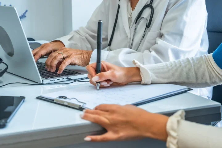 Clinician and researcher reviewing information on a laptop and clipboard, representing collaboration and real-world data used in biomedical research.